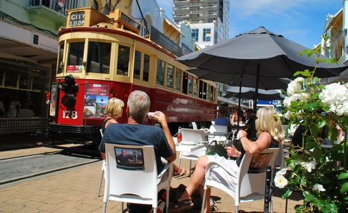 People relax at cafe as Christchurch Tram goes past 