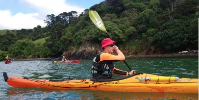 {Person in single kayak on the sea in front of cliffs and bay of Lyttelton Harbour