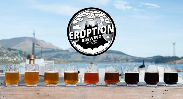 A line of glasses in front of Lyttelton Harbour with a logo for eruption brewery 