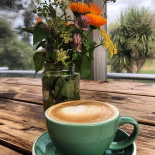cup of coffee in front of a jar of flowers