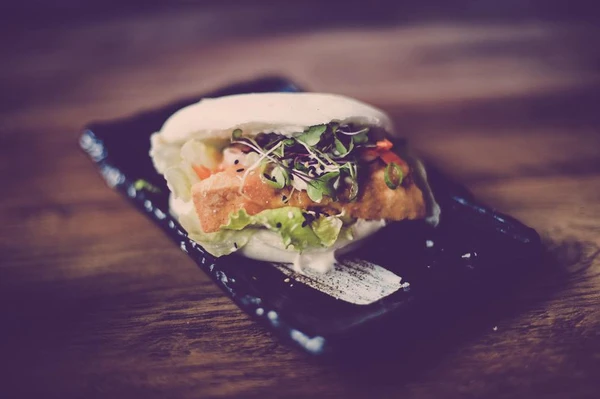 black plate with a bao bun filled with chicken on the table at super resturant