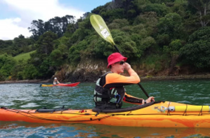 {Person in single kayak on the sea in front of cliffs and bay of Lyttelton Harbour