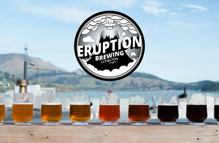 A line of glasses in front of Lyttelton Harbour with a logo for eruption brewery 